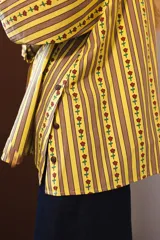 Camisa de manga larga con cuello clásico y cierre frontal de botones. Presenta un diseño de rayas verticales verdes y blancas con un estampado lineal de pequeñas flores rojas.