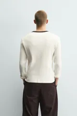 Camiseta de manga larga en tejido de punto canalé color crudo, con cuello redondo y tapeta frontal con botones en color marrón oscuro a contraste.