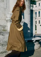 Trench coat de algodón en color verde oliva, con diseño largo y oversize. Presenta cuello camisero de pana, cierre de doble botonadura, cinturón con hebilla, trabillas en hombros y puños ajustables.