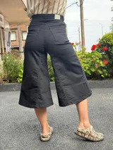 Jean capri negro de tiro alto con diseño de pierna amplia tipo culotte, confeccionado en denim con lycra, bolsillos y botón frontal.