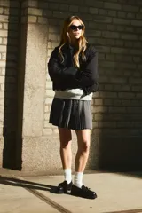 Pollera mini acampanada color gris oscuro, con tejido plisado, cintura elástica y cordón ajustable blanco y azul.