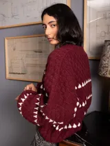 Buzo corto de tejido de punto en color negro, con diseño de textura en relieve y líneas horizontales blancas. Presenta cuello redondo y mangas largas con puños ajustados.