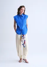 Camisa de popelín color azul, de diseño oversize y sin mangas, con cuello camisero, bolsillo parche delantero y cierre frontal con botones.