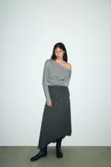 Camiseta de cuello barco y manga larga tipo murciélago, confeccionada en tejido de punto gris melange. Presenta detalle de tachas metálicas a lo largo de los hombros y las mangas.