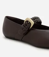 Chatitas de estilo bailarina en color marrón oscuro, confeccionadas en poliuretano. Presentan punta redondeada y una tira ajustable sobre el empeine con detalle de trenzado y hebilla metálica dorada.