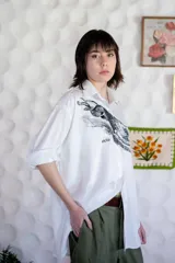 Camisa blanca de algodón con estampado de un galgo y la palabra "ocio" en el frente. Manga larga con puños y botones.