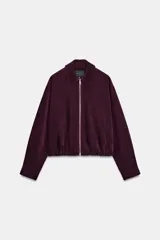 Cazadora bomber de Zara, de color bordó, con cuello de solapa, manga larga, bolsillos de vivo en el delantero y bajo elástico. Cuenta con cierre frontal de cremallera metálica.