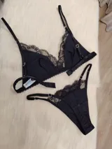 Conjunto de lencería compuesto por un corpiño triangular y una bombacha, ambos confeccionados en algodón negro con detalles de encaje en los bordes. El corpiño cuenta con breteles regulables y la bombacha presenta un diseño con tiras laterales.