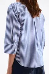 Camisa corta oversize de popelina de algodón con rayas verticales blancas y azules, cuello clásico, cierre frontal de botones, bolsillo en el pecho y mangas tres cuartos con puños anchos.