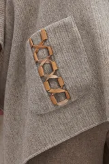 Poncho de lana color beige con cuello alto, bolsillos frontales y detalle de cordones de cuero en los bordes de los bolsillos.