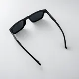 Lentes de sol polarizados con armazón gris translúcido y diseño rectangular, con detalle triangular negro en las patillas y cristales oscuros.