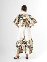 Conjunto de dos piezas confeccionado en viscosa con estampado floral en tonos marrones y verdes sobre base blanca. Incluye una blusa tipo camisa corta con cuello solapa, cierre frontal de botones y mangas abullonadas con diseño globo, y un pantalón tipo culotte de tiro alto, amplio y fluido con pinzas en la cintura.