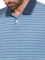 Polo Original Penguin de hombre con diseño a rayas horizontales en tonos de azul. Cuello y puños ribeteados en azul marino con detalle de línea blanca. Logo del pingüino bordado en el pecho. Corte slim fit.