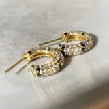 Aros tipo argolla pequeños de plata 925 con acabado en oro de 18k, con incrustaciones de circonitas multicolores. Cierre con perno a presión. Diámetro de 8,5 mm.
