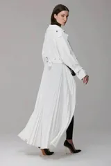 Mono largo de diseño minimalista con cuerpo superior tipo blazer cruzado de color blanco y parte inferior tipo calza ajustada de color negro. Presenta un cinturón integrado con mini bolsos tipo cartuchera y una falda plisada superpuesta en la parte trasera.