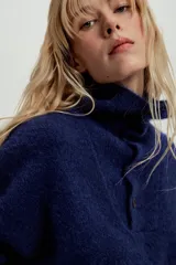 Jersey de punto de textura suave, color azul marino, con cuello perkins y cierre frontal parcial con botones. Presenta mangas largas con diseño holgado.