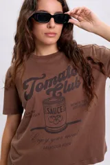 Remera marrón de manga corta y cuello redondo, con estampa frontal inspirada en la marca Tomato Club y textos alusivos.