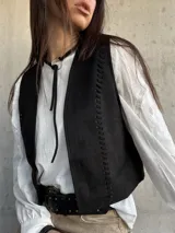 Chaleco negro de gamuza sintética, de estilo boho-chic, con costuras decorativas en los bordes y diseño clásico atemporal.