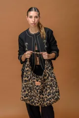 Bolso tipo hobo de gran capacidad con estampado animal print de vaca en tonos marrón y blanco. Presenta una etiqueta de cuero con el logo de la marca en el frente y un diseño de caída relajada.