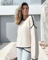Sweater de punto en color crudo con detalles de costuras y bordes en color negro. Presenta un diseño de corte holgado, cuello redondo y mangas largas con puños acanalados.