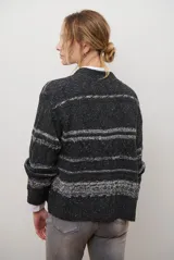 Sacon de tejido de punto grueso con diseño de ochos y rayas horizontales en contraste. Presenta cuello en V, cierre frontal con botones oscuros y mangas largas con puños acanalados.