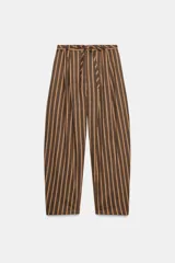 Pantalón de tiro medio con diseño tipo ballon, estampado a rayas verticales en tonos marrones y blancos. Presenta pliegues frontales, bolsillos laterales ocultos y cinturón del mismo tejido integrado en la cintura.