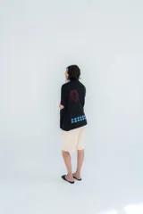 Cardigan de punto color marrón con cierre frontal, cuello alto y bolsillos aplicados. Presenta diseño tejido localizado con detalles en violeta y negro en el pecho.