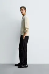 Pantalón de corte slim fit y color negro, confeccionado en tejido elástico. Cuenta con cintura elástica, trabillas, bolsillos frontales y cierre con cremallera y botón.