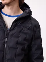 Campera puffer con capucha, color verde militar, con cierre frontal y bolsillos laterales. Presenta un diseño acolchado con costuras termoselladas y puños elásticos.