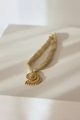 Collar dorado de cadena tejida con dije colgante en forma de caracola marina, hecho en acero quirúrgico hipoalergénico.