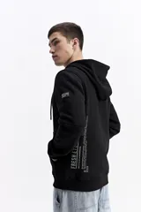 Campera con capucha y cierre frontal, color crema, con bolsillo canguro. Presenta un estampado de texto en el pecho y detalles en el puño.