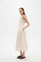 Vestido midi color beige claro, con cuello en V, sin mangas y corte entallado con pinzas.