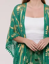 Kimono largo de viscosa color verde con estampado metalizado dorado de palmeras, mangas anchas, detalles de pompones en los bordes y diseño abierto.