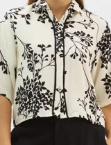 Camisa de corte holgado con estampado botánico en blanco y negro. Presenta cuello camisero, mangas cortas amplias y cierre frontal con botones y vivos a contratono.