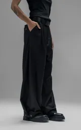 Pantalón sastrero de corte oversize, color negro, con pinzas frontales que forman tablones profundos, cintura ancha, presillas robustas y bolsillos laterales y traseros tipo ojal.