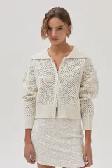 Cárdigan tejido de punto calado color crudo, con cuello polo, cierre metálico frontal y mangas largas.