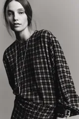 Camisa de manga larga con estampado a cuadros en blanco y negro. Presenta un cuello redondo y un pañuelo multiposición que cae en un drapeado asimétrico sobre el frente.