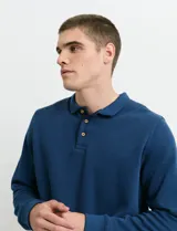 Remera de manga larga con cuello polo, confeccionada en tejido de punto canalé francés. Presenta abotonadura frontal con botones de madera y detalles a contratono en la cartera y el interior del cuello.