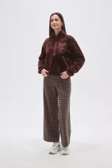 Buzo de polar tipo peluche color chocolate, con cuello alto y cierre frontal parcial. Presenta un bolsillo frontal con cierre y detalle de tela técnica en contraste.