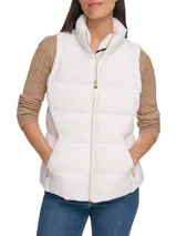 Chaleco blanco acolchado con cuello alto y cierre frontal con cremallera dorada. Tiene bolsillos laterales con cremallera y logo de la marca en el tirador.