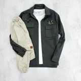 Sobrecamisa gris de gabardina con cuello clásico, cierre frontal con botones, dos bolsillos de parche con solapa en el pecho, mangas largas con puños abotonados y parches decorativos.