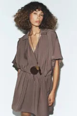 Collar de cordón fino negro con nudo, colgantes combinados de pieza metálica dorada, piedra ojo de tigre y cartera circular de piel 100% color marrón. Cierre con lazada y acabados con piezas metálicas doradas.