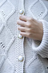 Saco tejido de punto con diseño de ochos y trenzas, color negro. Presenta cuello estilo camisero, cierre frontal con botones tipo joya, mangas holgadas y silueta oversize.