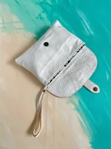 Sobre de mano de cuero blanco y amarillo, con solapa texturizada tipo cocodrilo y detalle de arte pintado a mano. Cuenta con cierre de broche imán y tira de mano.