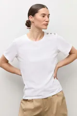 Remera blanca de manga corta con detalle de botones metálicos en el hombro, cuello redondo y corte clásico.
