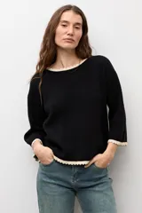 Sweater de punto negro con escote bote, mangas largas y detalles de terminación en ondas de color blanco en el cuello, los puños y el ruedo.