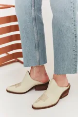 Mule de cuero color suela con diseño de punta fina y bordado decorativo en el empeine. Presenta un taco bajo de madera y una silueta abierta en el talón.