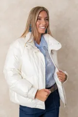 Campera puffer de acabado satinado en color beige, con cuello alto, cierre frontal y bolsillos laterales. Presenta un diseño moderno y sofisticado.