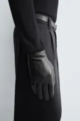 Guantes de cuero negro con interior forrado en tejido de punto. Presentan costuras decorativas en el dorso y tecnología táctil en los dedos para el uso de dispositivos móviles.
