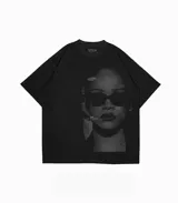Remera oversize negra con estampado en blanco y negro de Rihanna usando anteojos de sol. Presenta texto en la parte superior izquierda y texto pequeño en la parte inferior derecha.
